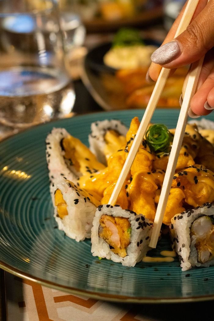 Close-up of a hand holding chopsticks with sushi roll, highlighting deliciousness.