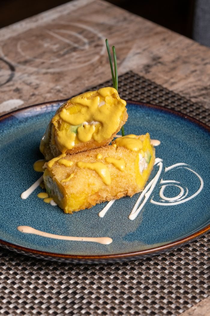 A gourmet fried sushi roll topped with creamy sauce, served on a blue plate.