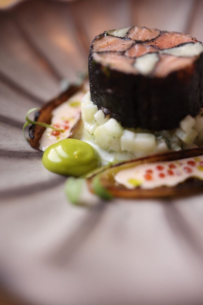 Close-up of a gourmet salmon dish artfully presented with green sauce and garnish.