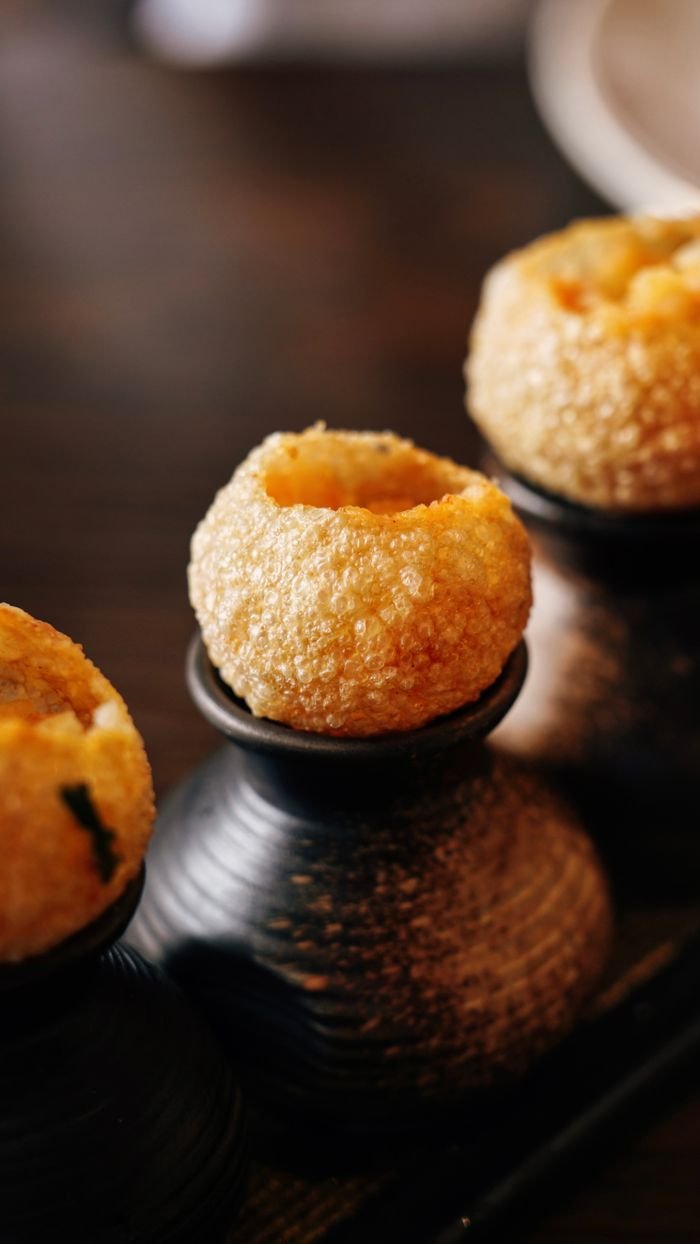 Macro shot of savory Indian street snack, Pani Puri, on wooden platter.