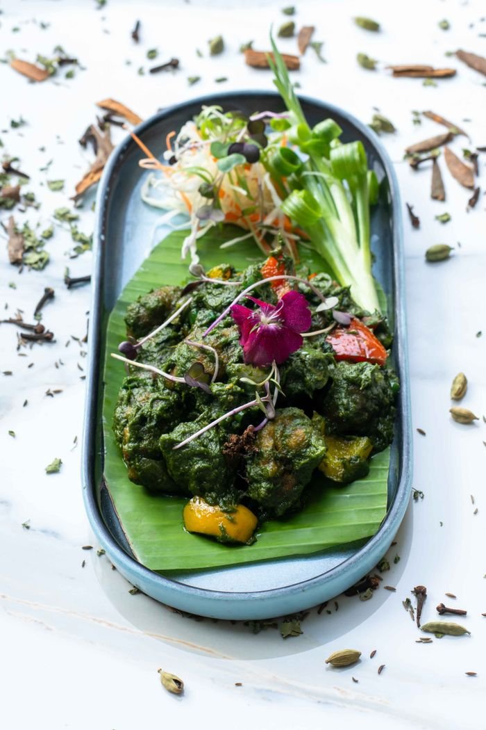 Vibrant plate of sautéed vegetables and edible flowers on a banana leaf, garnished with microgreens.