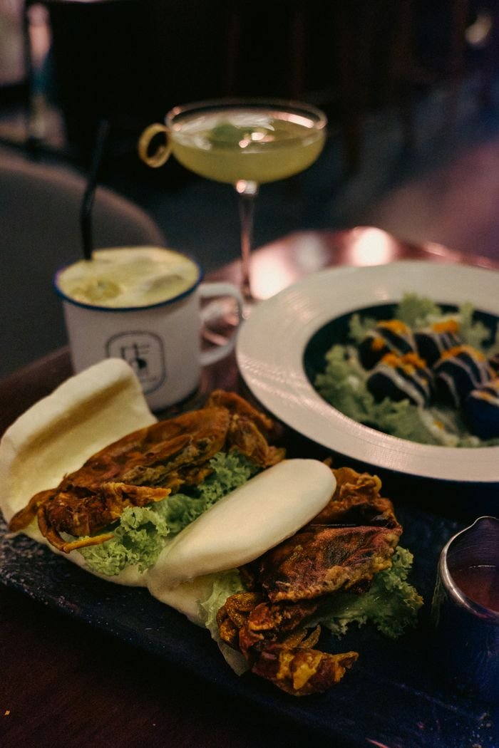 Gourmet Asian fusion dish with bao buns and soft shell crab paired with elegant cocktails.
