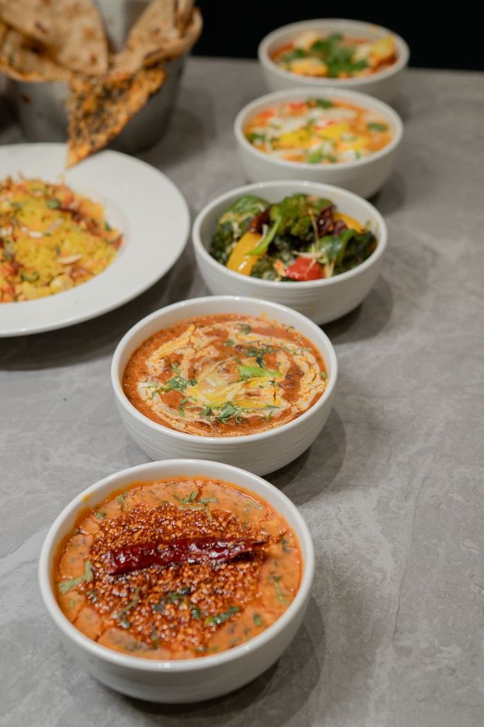 A variety of Asian-inspired dishes presented in bowls on a gray stone surface, highlighting vibrant colors and spices.