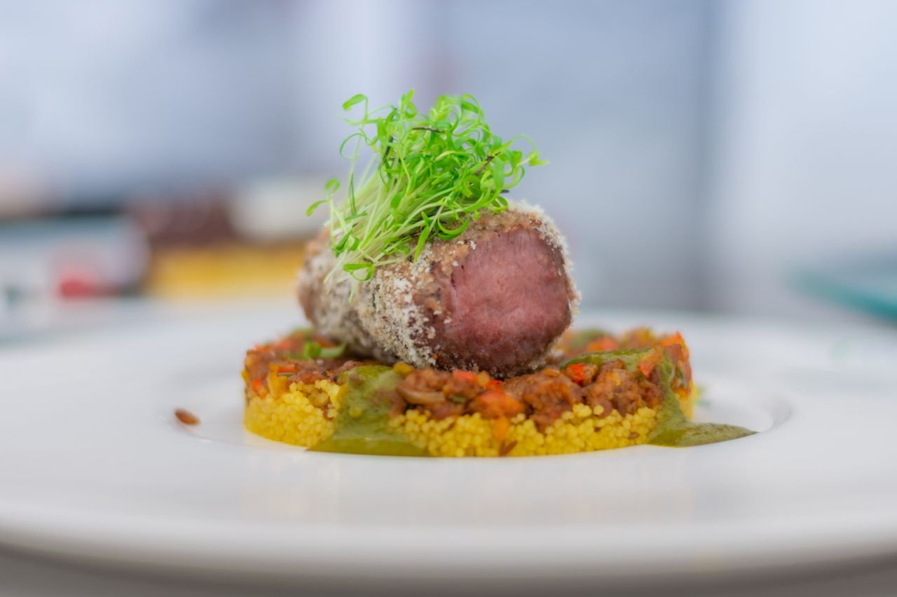 Close-up of a gourmet lamb dish with couscous and microgreens, exquisitely plated.